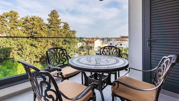 A balcony with a round table and four chairs, overlooking a residential area with trees and buildings. - Casino & Mall Jacuzzi Penthouse (Lemesos)