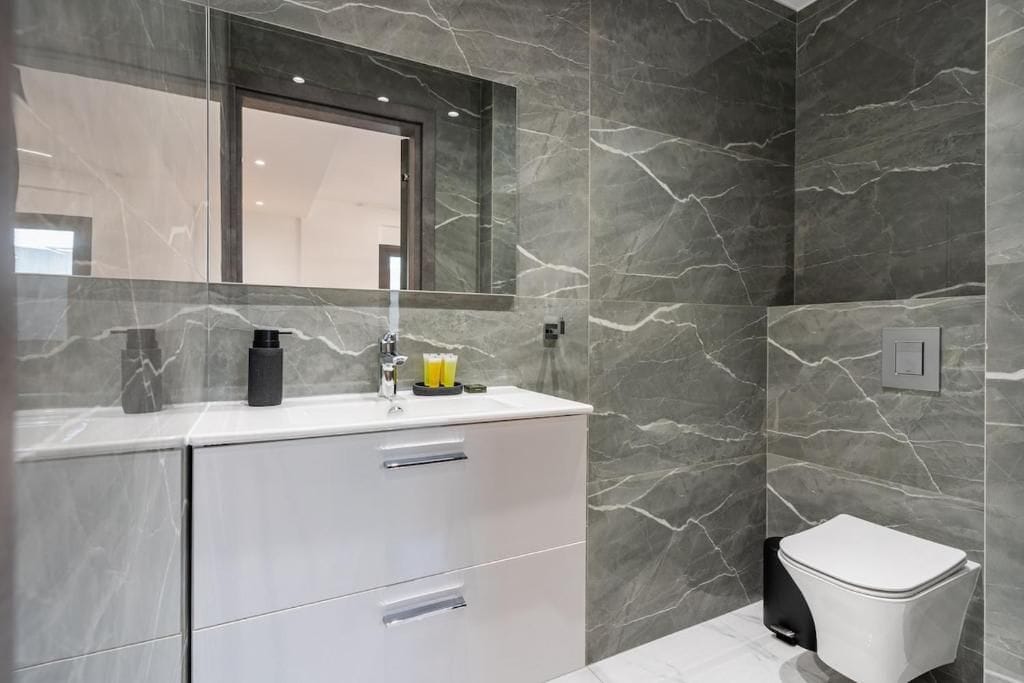 Un baño moderno con un lavamanos de mármol, un espejo y un inodoro.