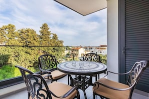 Uma varanda com uma mesa redonda e quatro cadeiras, com vista para uma área residencial com árvores e edifícios.