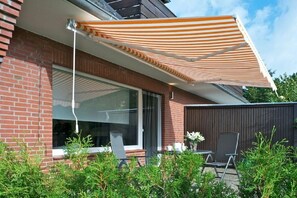 A modern house with a brick exterior, a large window, and a patio area with a table and chairs. - Holiday apartment with 1 bedroom (St. Peter - Ording)