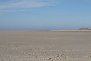 A wide, flat beach with a distant lighthouse. - Holiday apartment with 1 bedroom (St. Peter - Ording)