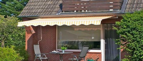 A patio with a table and chairs, a small garden, and a building with a sloped roof.
