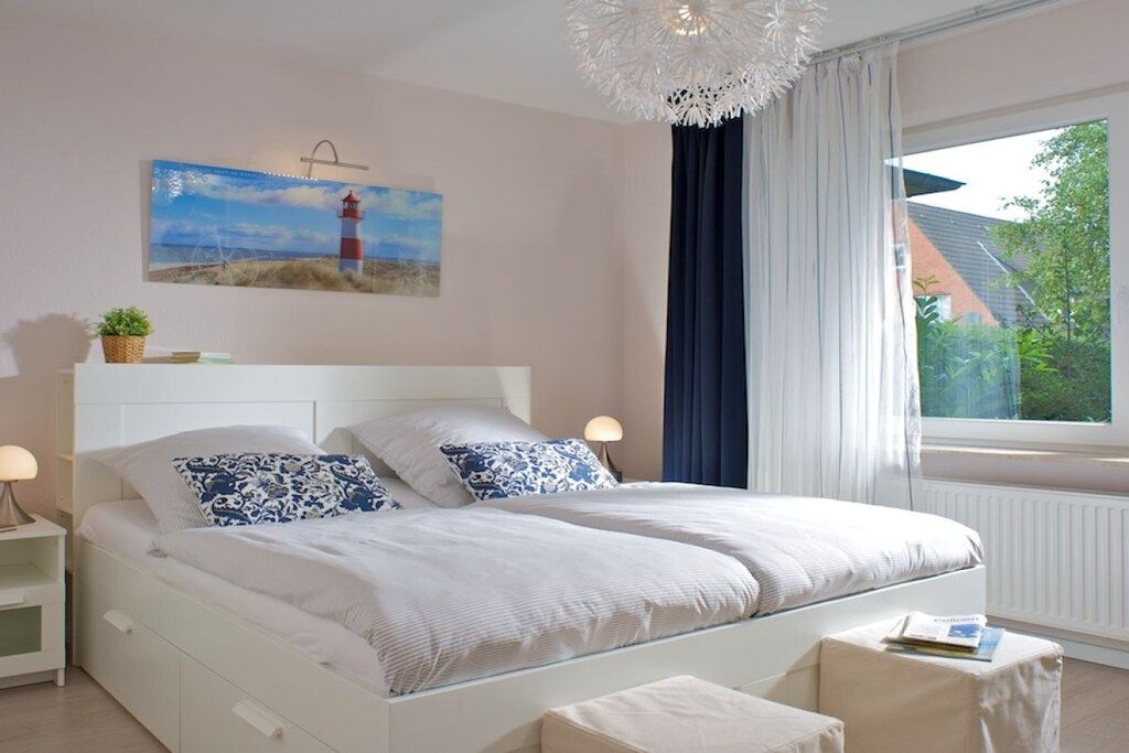 Ein Schlafzimmer mit einem Bett, Nachttischen, einer Lampe, einem Fenster mit Vorhängen und einem Bild an der Wand.