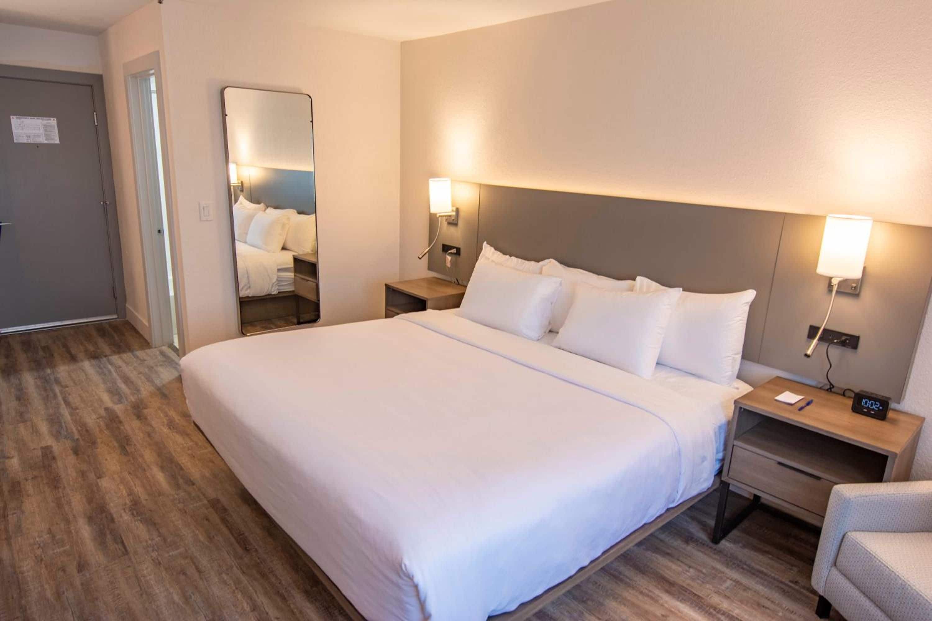 Ein Hotelzimmer mit einem großen Bett, Nachttischen, einem Beistelltisch, einem Sessel und einem Spiegel.