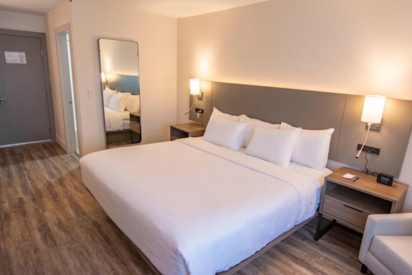 A hotel room with a large bed, bedside tables, a nightstand, a chair, and a mirror.