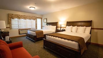 A hotel room with two beds, a desk, a chair, and a window with blinds.