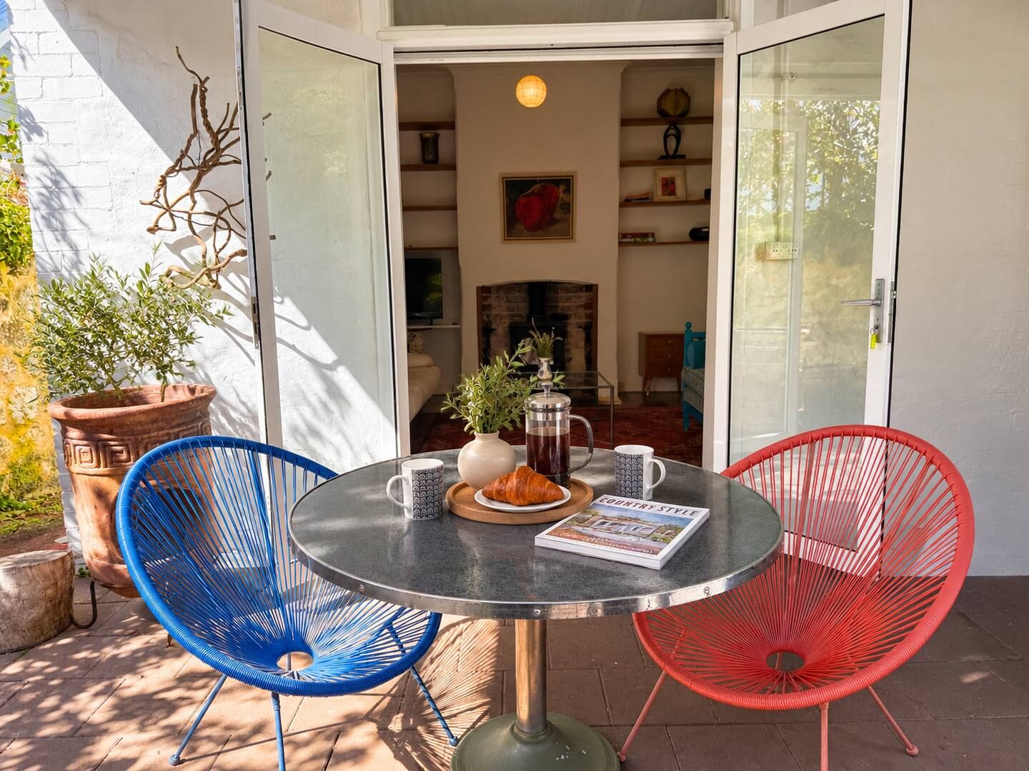 An open patio with a round table, two chairs, a potted plant, a book, and a coffee pot.