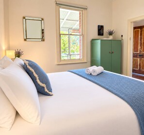 A neatly made bed with pillows and a rolled towel, a green cabinet, a window with a view, and a door. - Tucked away in a quiet pocket near Fremantle, this character-filled private garden cottage comfortably sleeps 2. Enjoy morning coffee on the sunny front verandah, relax among lavender and vines in the leafy fenced garden, and stroll into Freo’s cafés (Beaconsfield)
