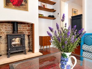 A living room with a fireplace, a blue sofa, and a vase with purple flowers. - Tucked away in a quiet pocket near Fremantle, this character-filled private garden cottage comfortably sleeps 2. Enjoy morning coffee on the sunny front verandah, relax among lavender and vines in the leafy fenced garden, and stroll into Freo’s cafés (Beaconsfield)
