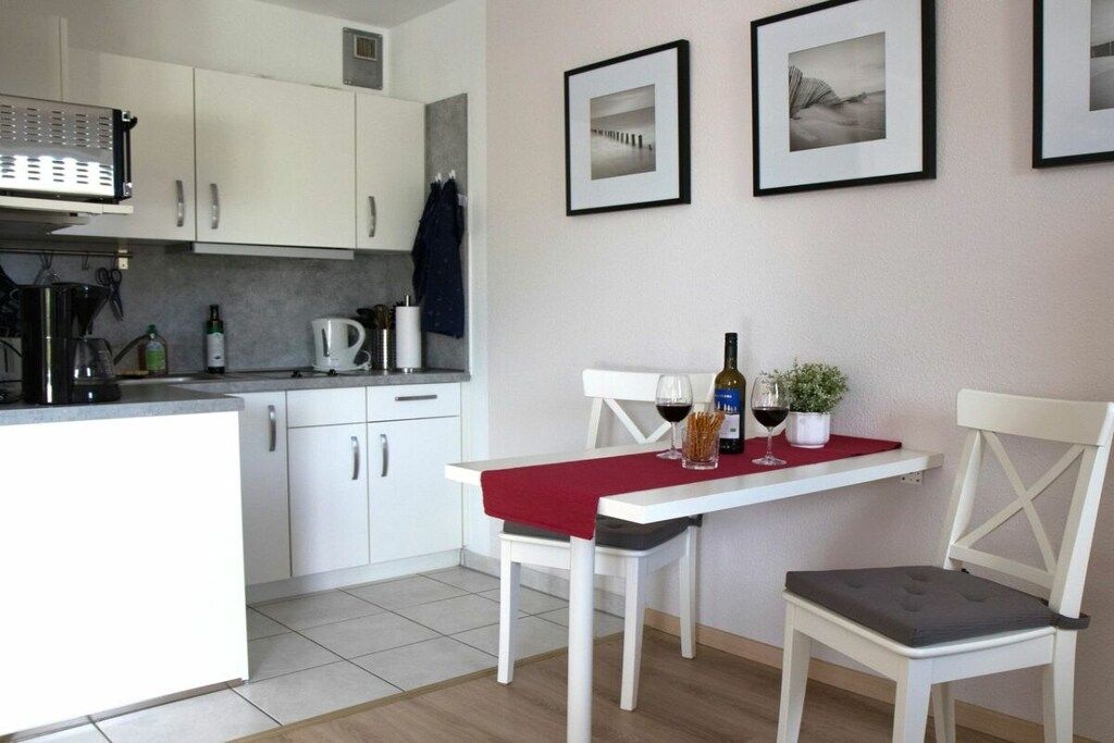 Une cuisine de taille réduite avec des meubles blancs, une machine à café et une nappe rouge.