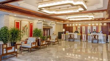 Un hall de hotel con mostrador de recepción, zona de estar y plantas decorativas.