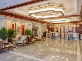 A hotel lobby with a reception desk, seating area, and decorative plants.