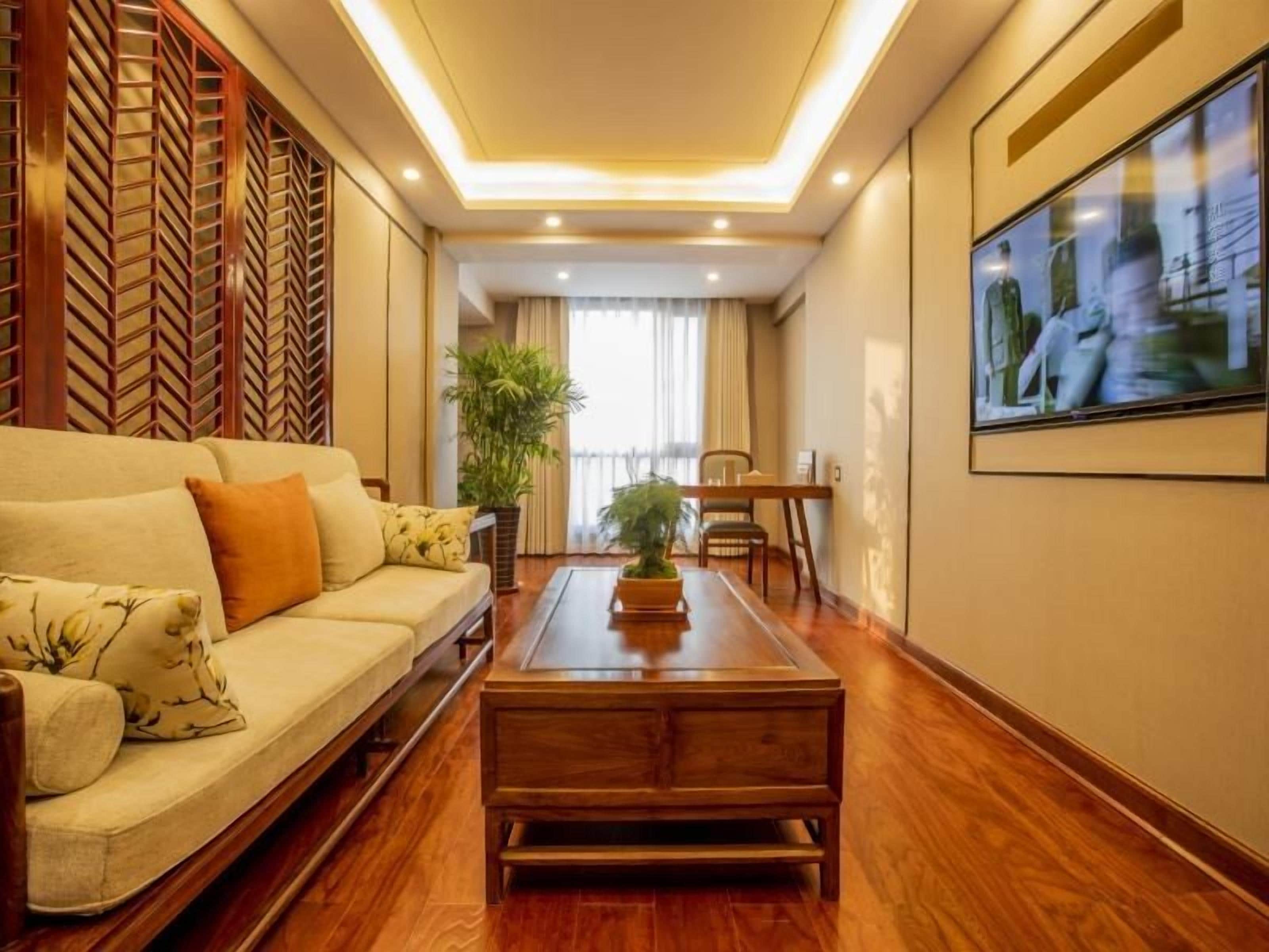A hotel room with a sofa, a coffee table, a television, and a plant.