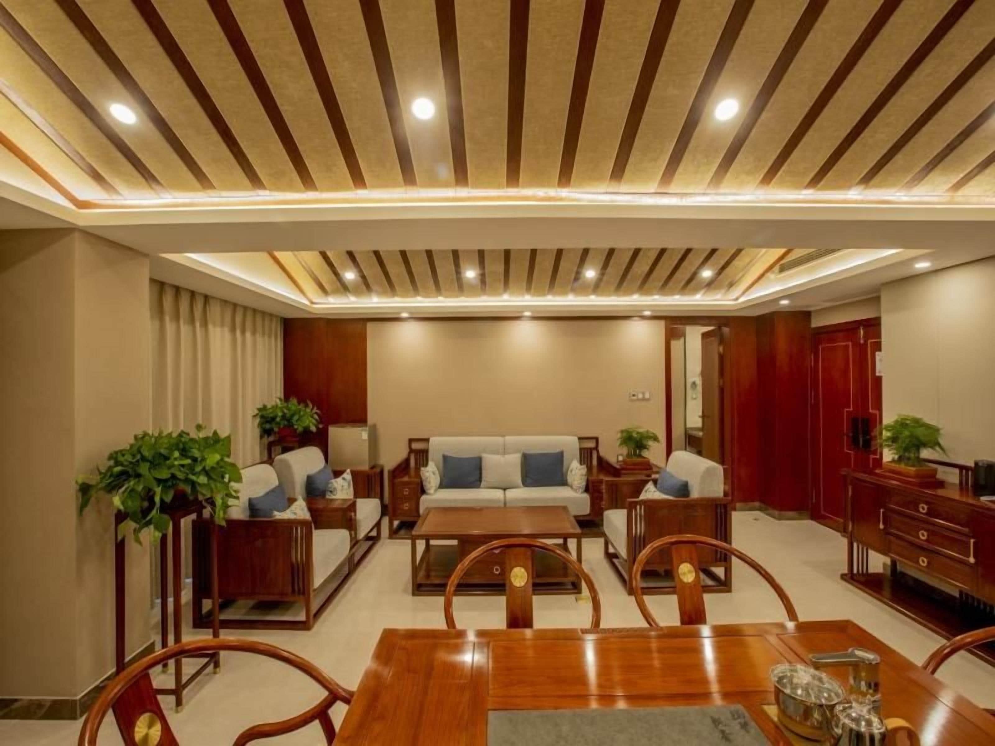 A modern living room with a sofa set, dining table, and chairs, wooden flooring, and recessed ceiling lighting.