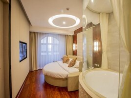 A hotel room with a bed, a large bathtub, and a window with curtains.