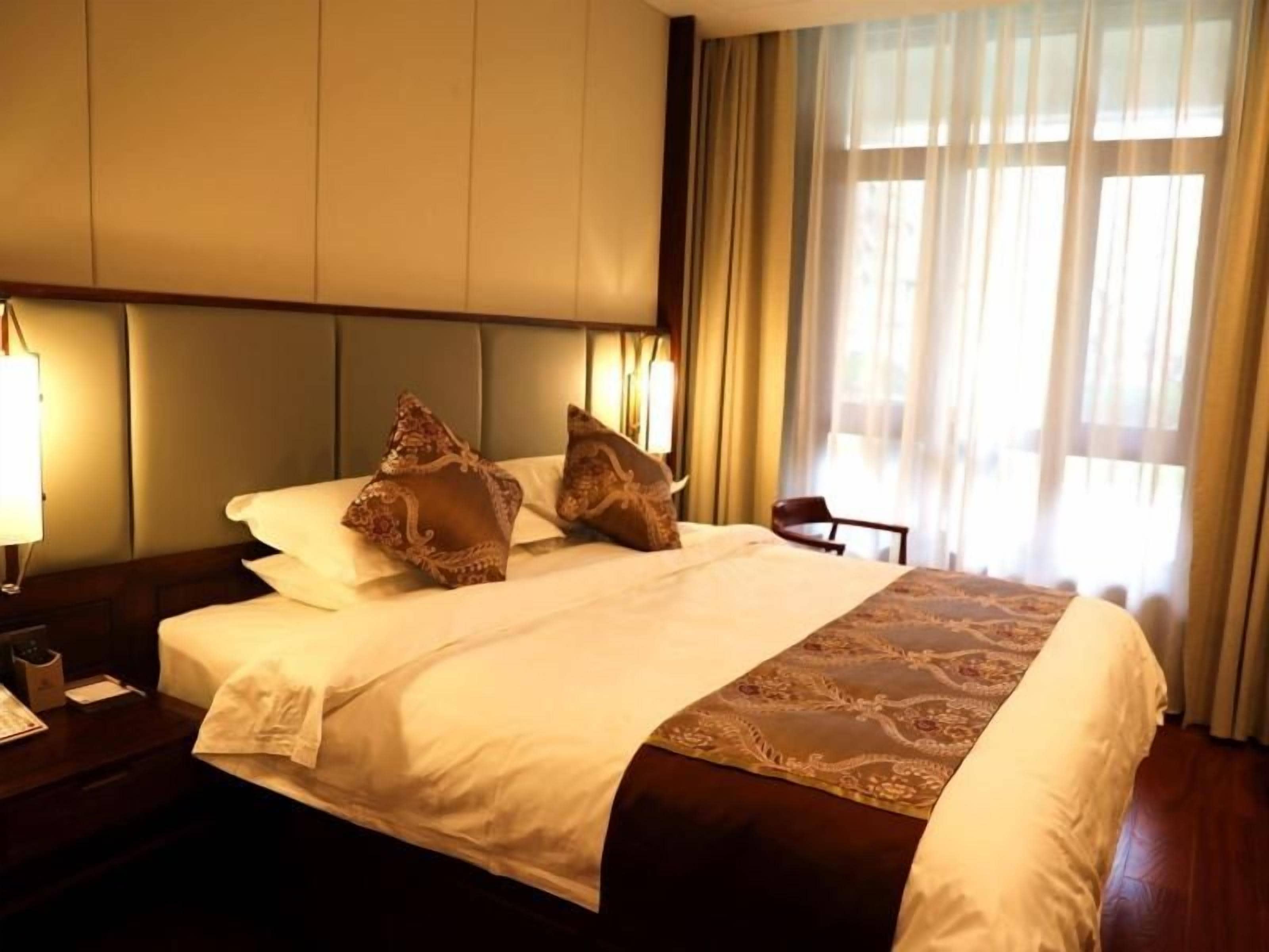 A hotel room with a large bed, a nightstand with a lamp, and a window with curtains.