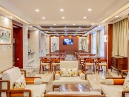 A hotel lobby with a long reception desk, multiple seating areas, and a television screen.