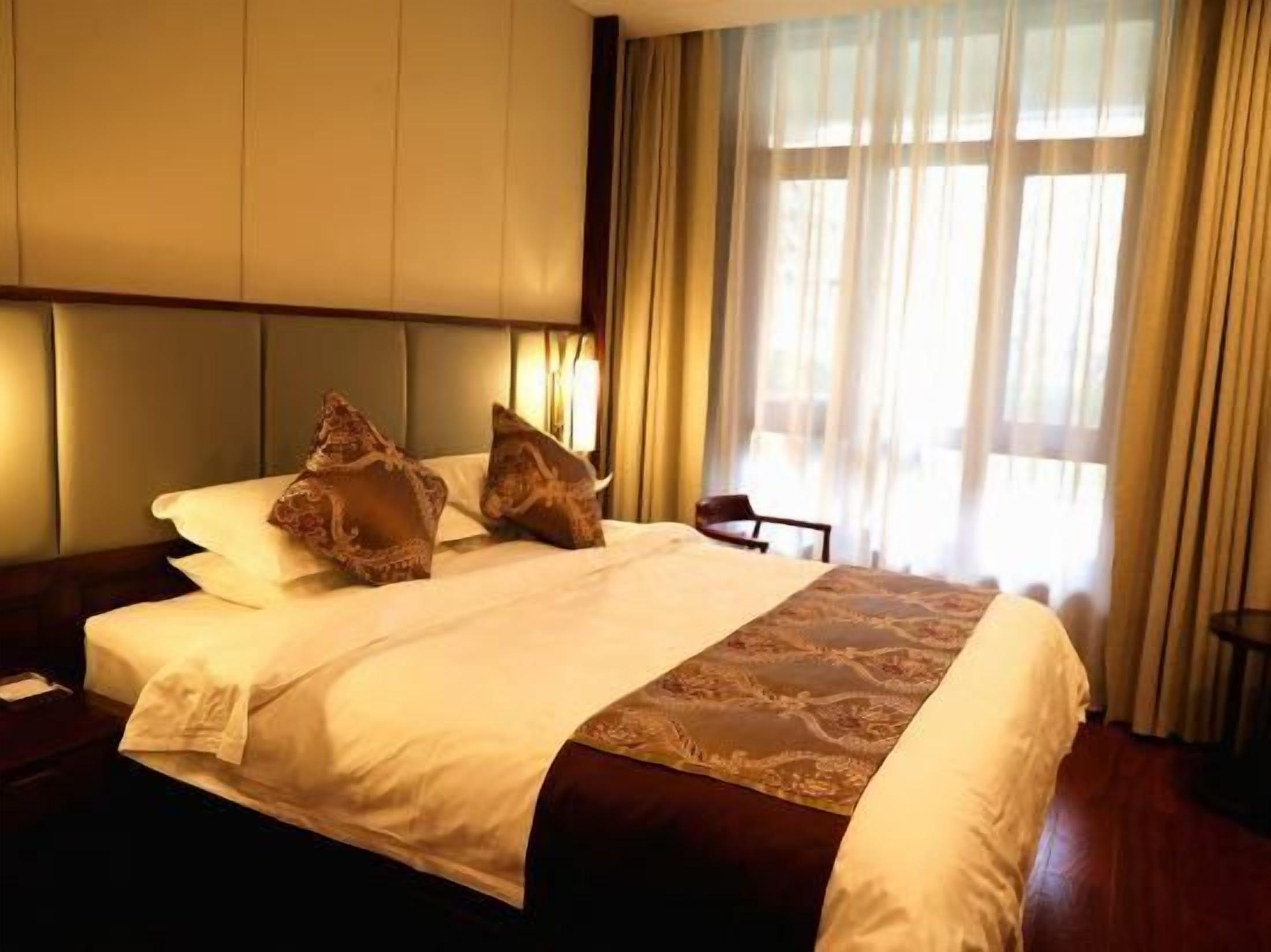 A hotel room with a large bed, a headboard, and a window with curtains.