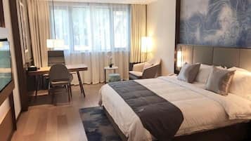 Una habitación de hotel con cama, escritorio, silla y un ventanal con cortinas.