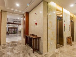 A hotel lobby with marble flooring, a reception desk, and an elevator.