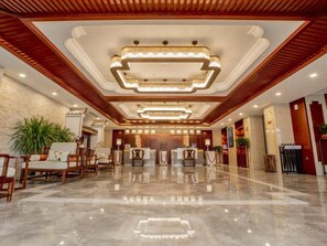Un hall de hotel con piso de mármol pulido, paneles de madera en el techo y un mostrador de recepción con sillas.