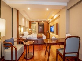 Una habitación de hotel con cama, escritorio, silla, mesita y televisor.
