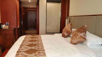 A hotel room with a bed, pillows, a bedside table, and a door leading to a hallway.