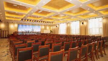 A conference room with rows of wooden chairs, a large screen at the front, and a carpeted floor.