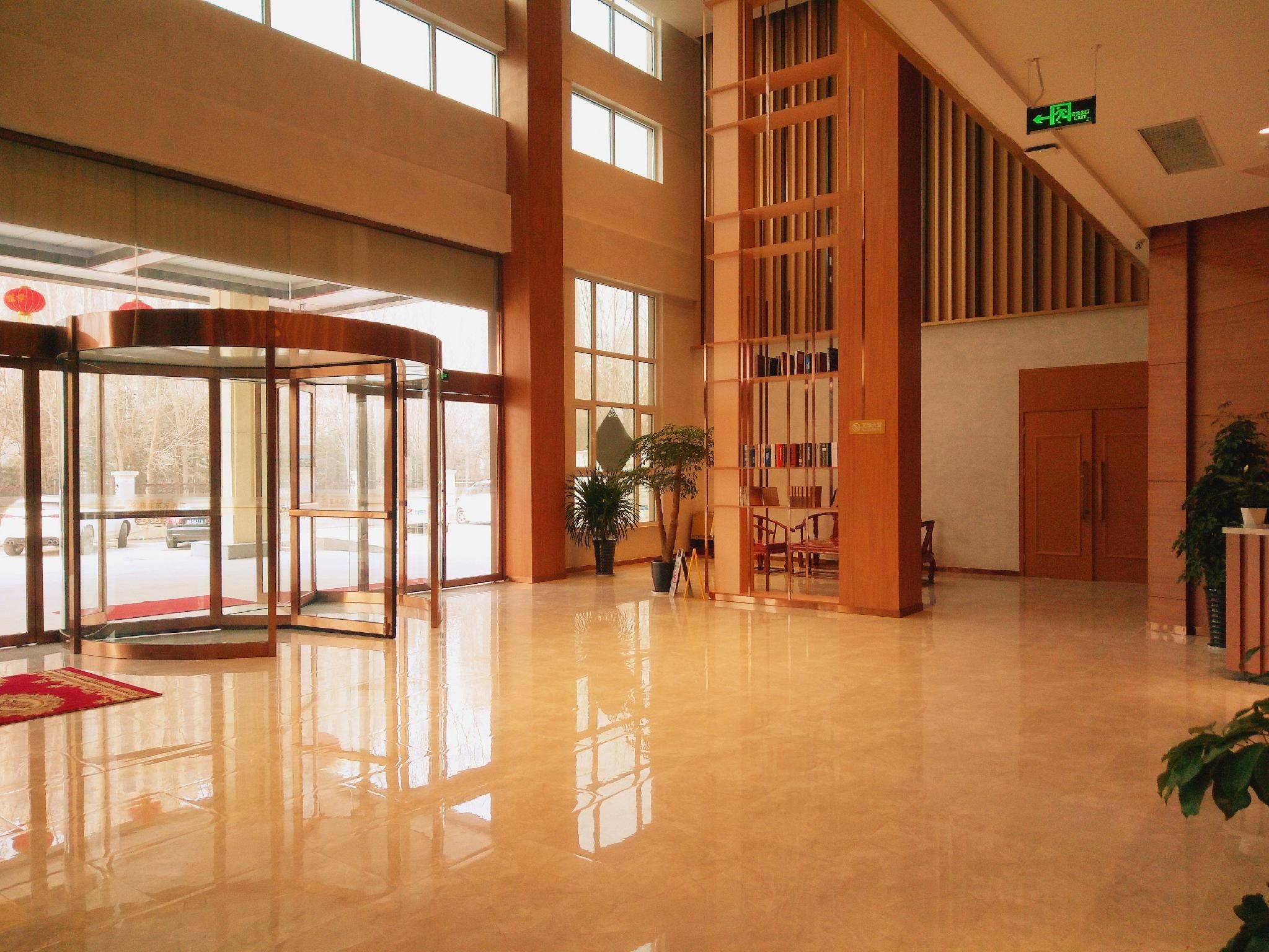 A spacious lobby with a revolving door, a large bookshelf, and a potted plant.