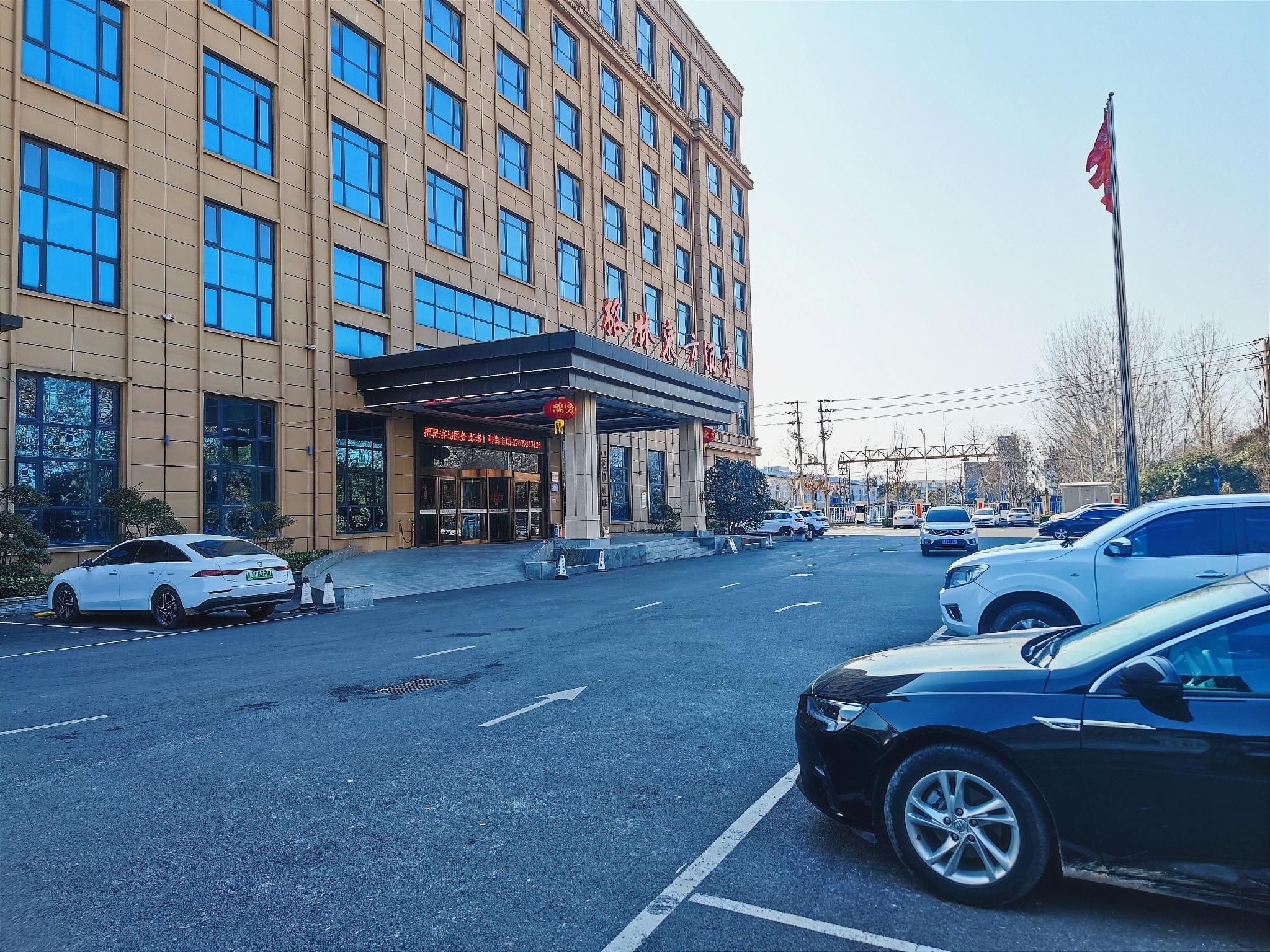 A hotel with a modern facade, multiple floors, and a parking lot with several cars.
