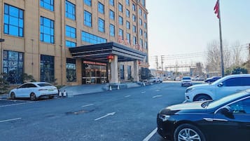 A hotel with a modern facade, multiple floors, and a parking lot with several cars.