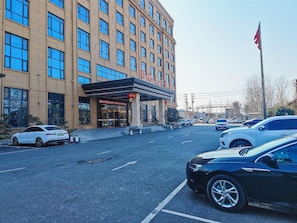 A hotel with a modern facade, multiple floors, and a parking lot with several cars.