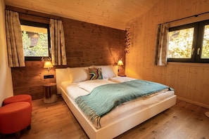 A wooden-paneled bedroom with a bed, two bedside lamps, and a window with curtains. - Superior Chalet # 56 with Sauna & Hot Tub (Turrach)