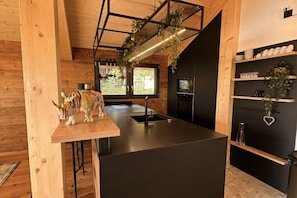 A modern kitchen with a wooden island, black cabinetry, and a window with a view of greenery. - Superior Chalet # 56 with Sauna & Hot Tub (Turrach)