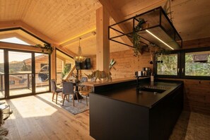 A modern kitchen with a central island, wooden walls, and a large window overlooking a mountainous landscape. - Superior Chalet # 56 with Sauna & Hot Tub (Turrach)