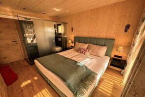 A wooden-paneled room with a bed, a nightstand, and a bathroom door. - Superior Chalet # 56 with Sauna & Hot Tub (Turrach)