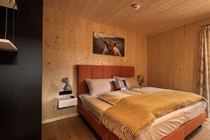 Un dormitorio con cabecera de madera, cama con manta color beige, mesita de noche con lámpara y un cuadro de un toro en la pared.