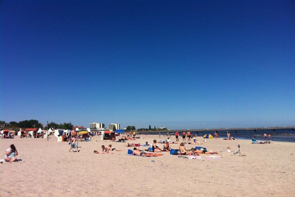 A beach with people sunbathing and swimming, umbrellas, and beachside buildings.