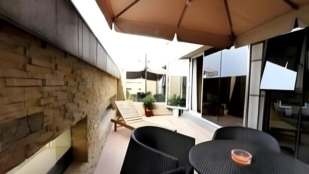 Un espace patio avec des sièges d’extérieur, un mur en pierre et un bâtiment moderne en arrière-plan.