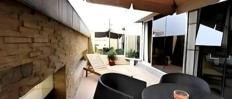 Un patio con mobiliario exterior, un muro de piedra y un edificio moderno al fondo.
