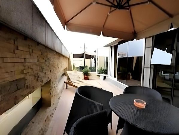 A patio area with outdoor seating, a stone wall, and a modern building in the background. - Ji Hotel (Changsha)