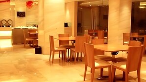 Un espace repas moderne avec un sol en marbre, des tables et des chaises en bois, et une cloison en verre qui sépare l’espace repas de la cuisine.