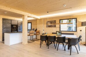 A modern kitchen with a central island, wooden walls, and a dining area with black chairs.
