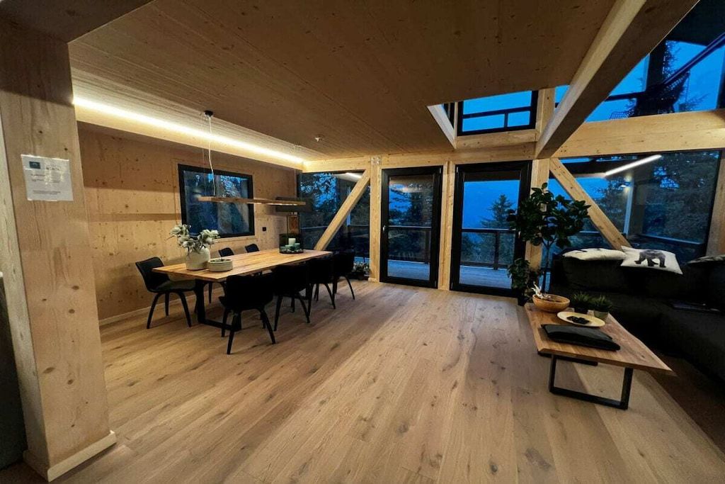A modern interior with a wooden dining area, a sofa, and large windows.