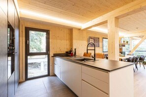 Ett modernt kök med en stor köksö, träpanel i taket och utsikt genom dörren.