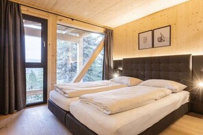 A bedroom with two beds, wooden walls, a large window, and framed pictures on the wall.