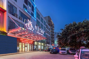 A hotel with a prominent neon sign, multiple floors, and a parking lot with cars.