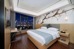 A modern hotel room with a large bed, a desk, and a view of a cityscape at night. - Junting (Chongqing)