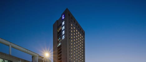 A high-rise hotel with a prominent 'L' sign, surrounded by urban buildings and streetlights.