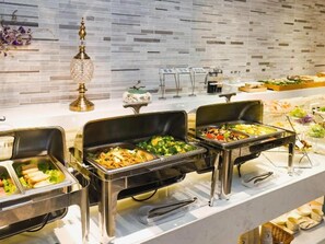 Een buffetopstelling met meerdere stations, waaronder schalen met salades, groenten en andere gerechten.